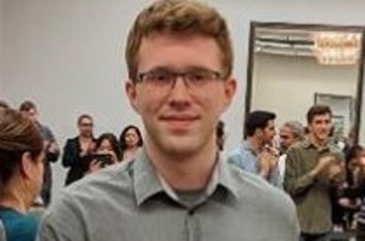 Anthony Trufanov standing next to award shaped like pyramid in busy room 