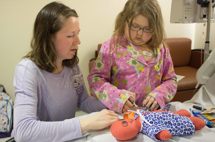 Child Life Specialist Ashley Rapske helps young Shannon understand how IVs work by practicing on a doll.