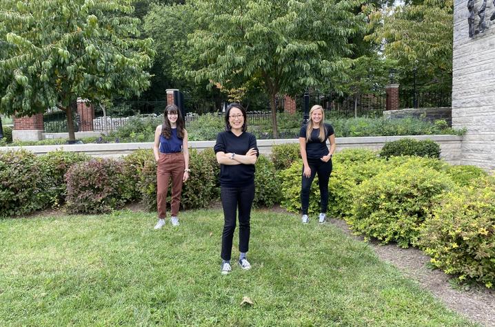 photo of Sam-Claire Bieber and Haydon Gains standing behind Yoon Bae on lawn in front of Fine Arts Building