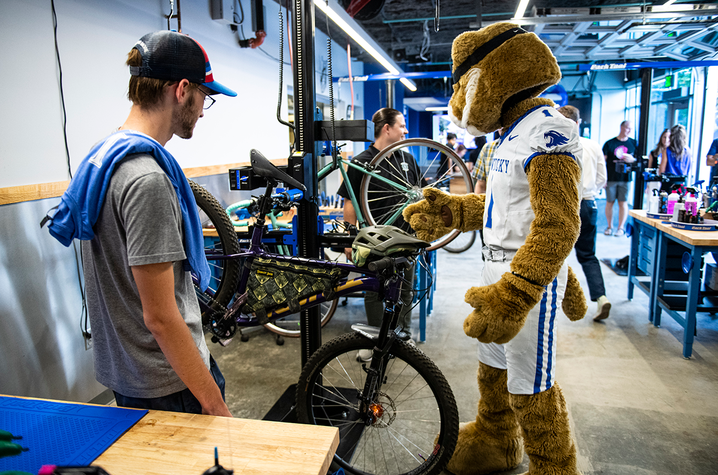 Mascot Visits Campus Bike Workshop Person and university mascot examine a bicycle in a bike repair workshop.