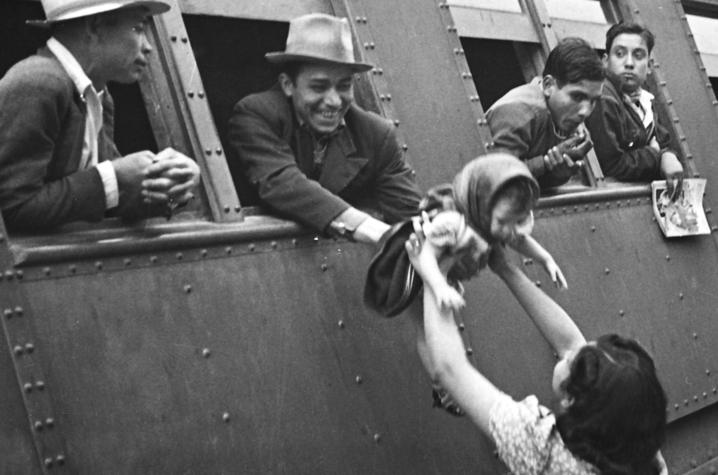 black and white photo of man passing baby out of train window to woman - Braceros Photo Exhibit 