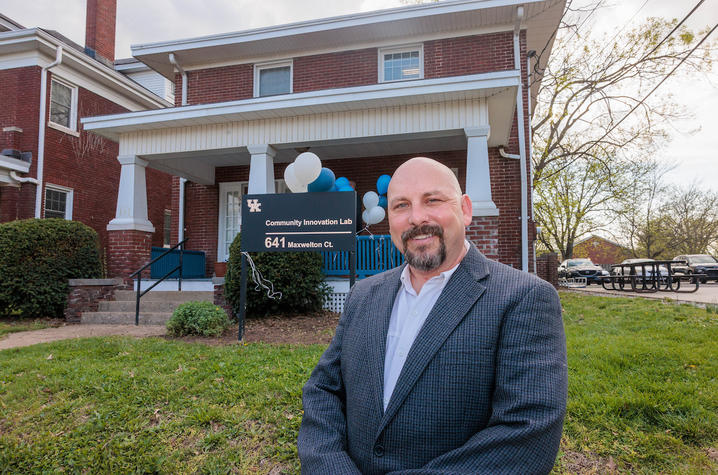 photo of Bryan Hains A person stands outside a brick campus building near an entrance sign, with the building and surrounding lawn visible in the background.