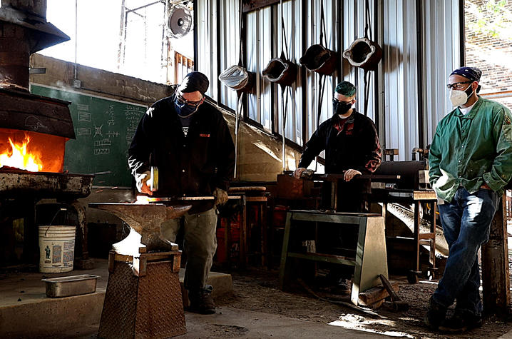 Photo of Jeremy Colbert forging a piece of metal while two other men watch