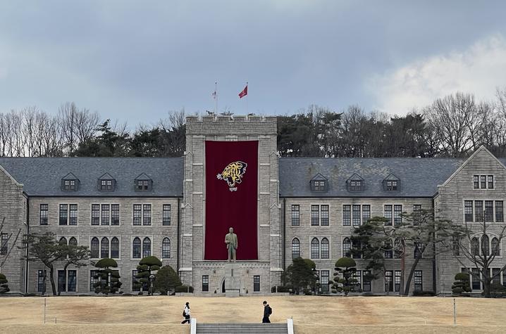 Large campus academic building with a central red banner featuring a white wildcat logo, set in front of a wide lawn under a cloudy sky.