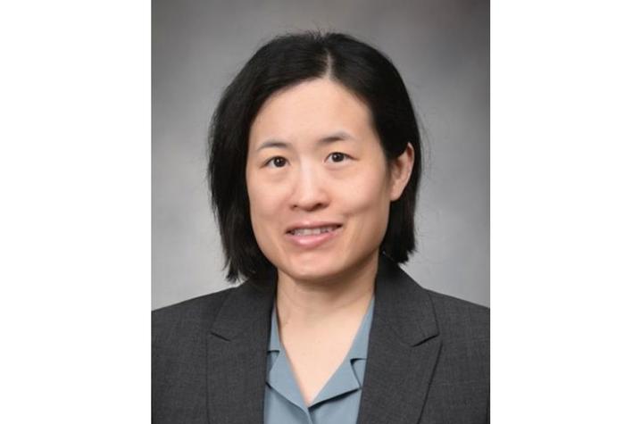 Photo of Helen Wei Professional headshot of a person with short dark hair wearing a gray blazer and light blue collared shirt, posed against a gray studio background.