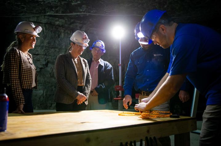 People wearing hard hats gather around a table during a demonstration inside an underground mine. People wearing hard hats gather around a table during a demonstration inside an underground mine.