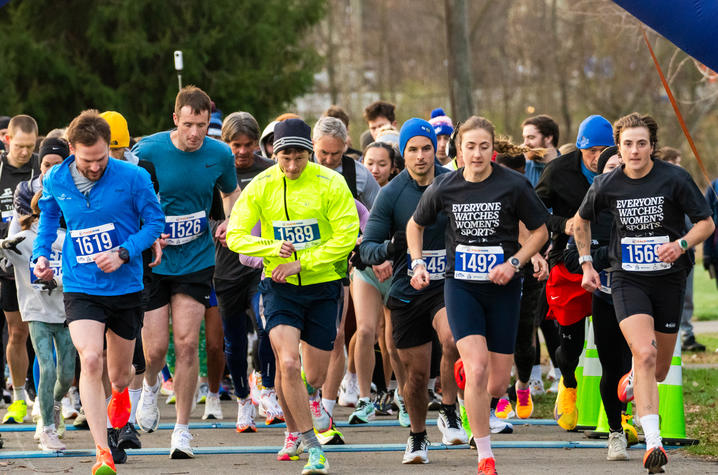 Image of a group of runners at the third annual World Hearing Day 5K A group of runners takes off from the starting line of an outdoor race, wearing numbered bibs and cool‑weather athletic gear.