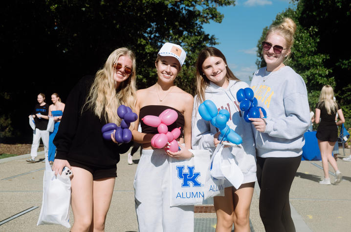 Four people stand outdoors holding colorful balloon creations, including flowers and an animal-shaped balloon.