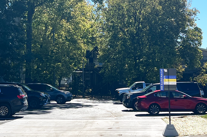 Cars parked in a tree-lined lot, with a University of Kentucky parking sign near the entrance.