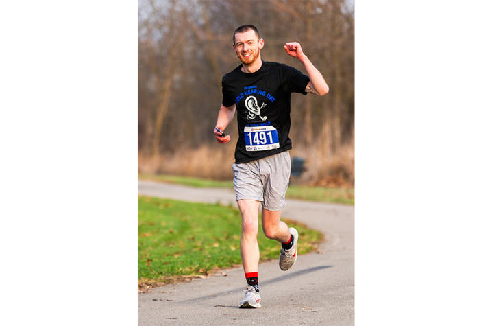 Photo of Evan Smith at the World Hearing Day 5K image of young man running a race and smiling at the camera