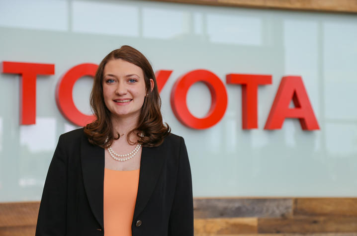 a smiling person stands in front of a Toyota sign