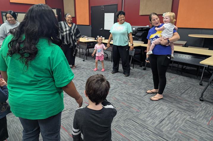 Parents standing around in a circle with three children. One person is holding a baby and the other two children are standing next to adults. 