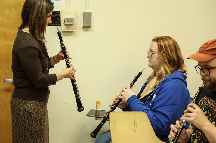Music instructor demonstrates oboe technique to seated students.