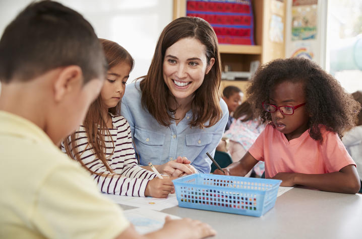 photo of teacher visiting with 3 elementary school kids at table