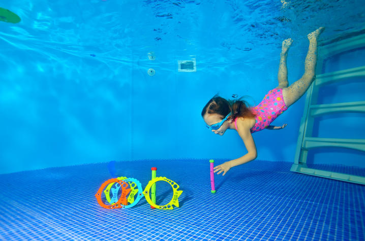 child in bright pink bathing suit diving for rings underwater in pool