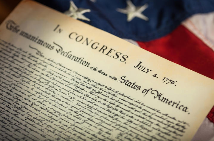 Close-up of the Declaration of Independence with an American flag in the background.