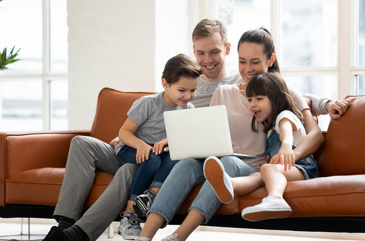 family sitting on sofa looking at laptop computer