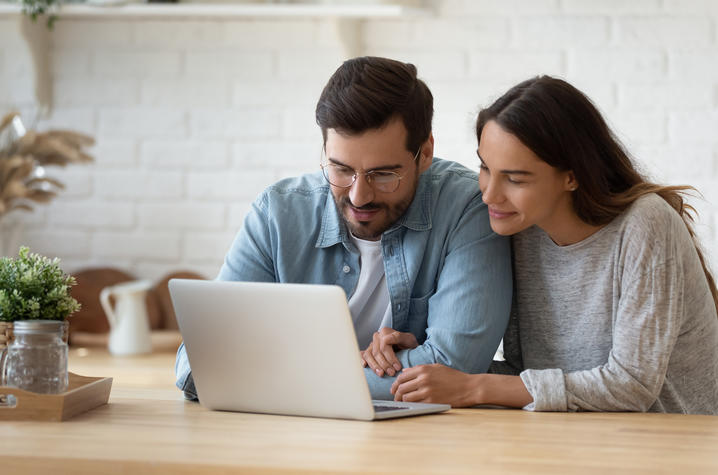 Couple seated at wooden table looking at laptop