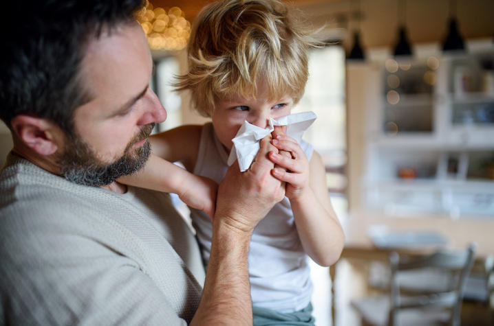image of father helping young son blow his nose into a tissue.
