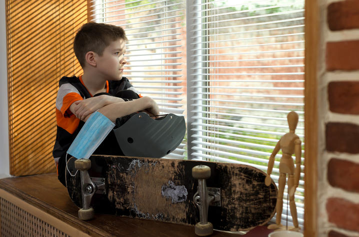stock photo of boy sitting in windowsill with skateboard, helmet and mask in hand