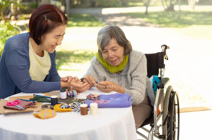 young woman sitting with old woman in wheelchair doing crafts