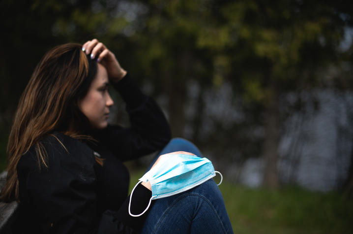 photo of young woman outside coping with stress of social isolation, face mask on knee