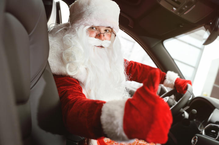 Santa Claus sitting behind the wheel of a car shows a thumbs up
