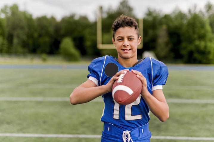 image of male-presenting adolescent in blue football jersey holding football