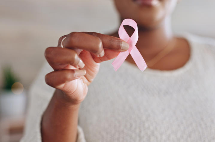 Pink awareness ribbon Close-up of a person holding a pink ribbon in front of a white shirt.