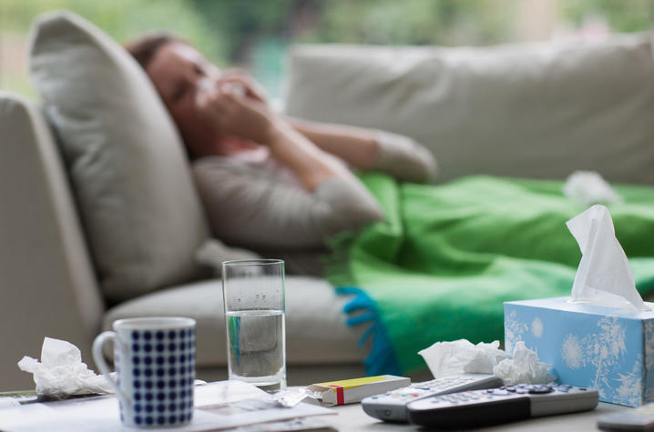 Sick woman laying on sofa blowing nose 