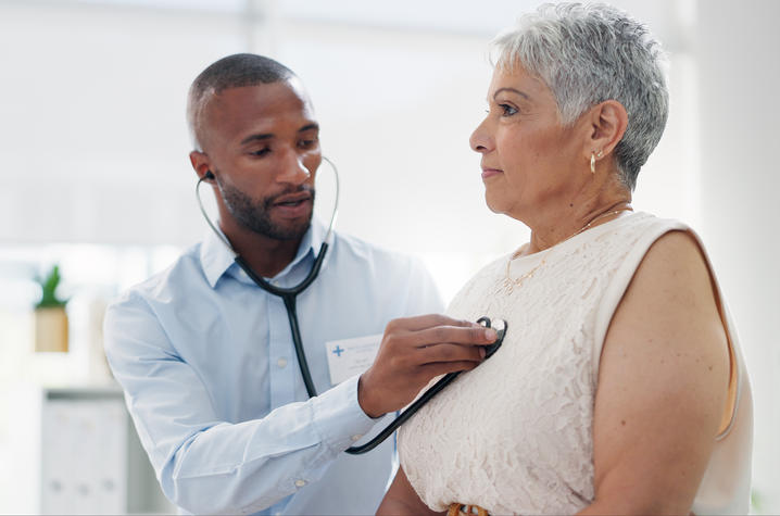 A doctor uses a stethoscope to listen to an older woman’s chest during a medical exam in a bright clinic room.