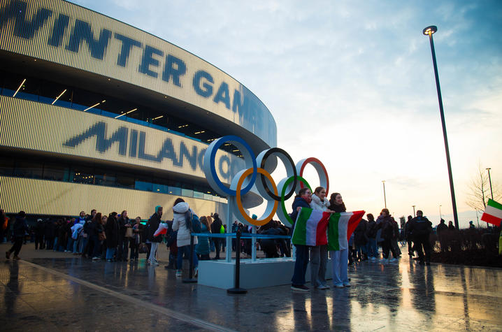 People making photos near the 5 rings symbol outside Arena Santa Giulia during the Milano Cortina 2026 Olympic Winter Games in Milan. Background with copy space at sunset.