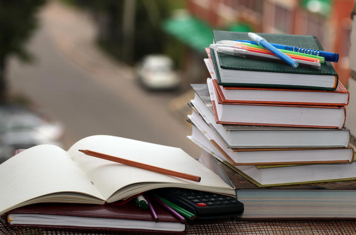 photo of books stacked on a desk with pens and calculator