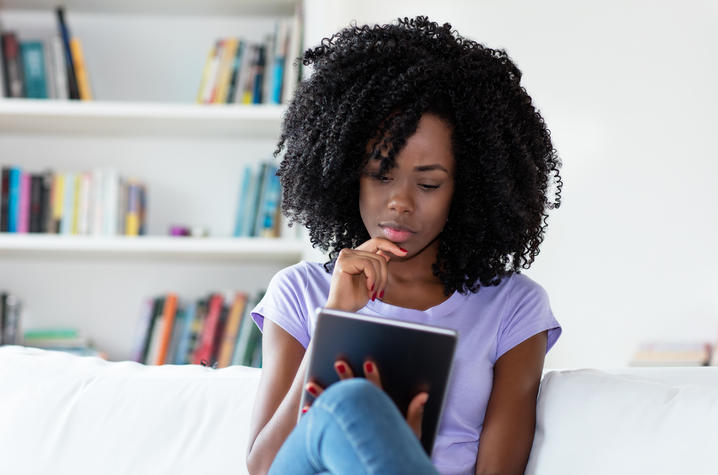 photo of African American woman sitting on couch reading newspaper online