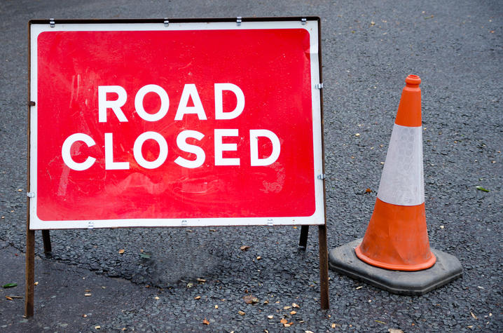 sign of road closed with a traffic cone setting beside it