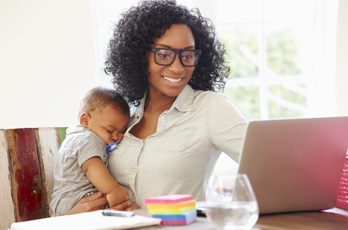 photo of woman working from home while holding a baby