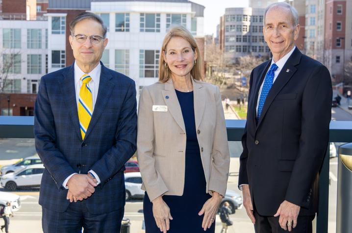 Three professionally dressed adults standing outdoors on a terrace with campus buildings visible in the background