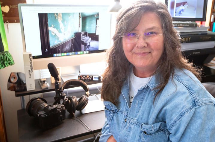 Terry in the studio A researcher sits at an office workstation with a camera, microphone, headphones and computer displays showing images of historic interiors. The workspace reflects efforts to document, preserve and study cultural heritage sites.
