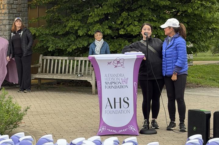 A speaker addresses participants at a podium with rows of purple water bottles displayed in the foreground.