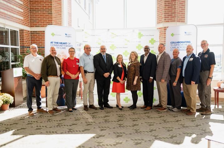 photo of Gill Affiliate Network A group of 13 people stands together in front of Fleming County Hospital and UK HealthCare Gill Heart & Vascular Institute banners during an indoor event.