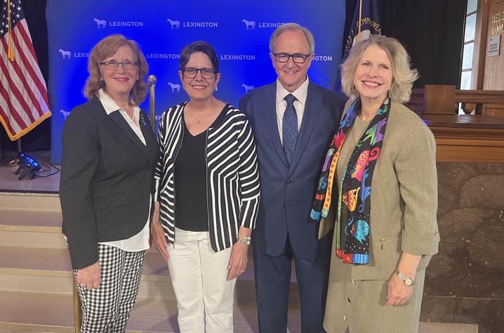 Image of four people standing against a blue backdrop