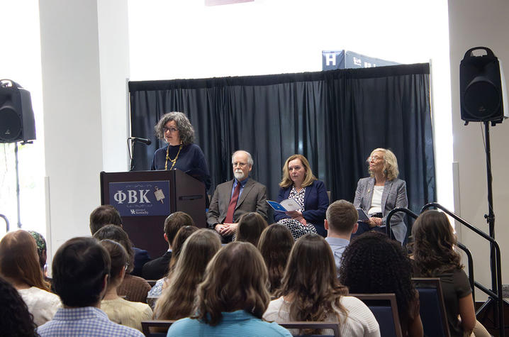 Panel of four speakers seated at a stage with a Phi Beta Kappa podium, facing an audience in a large indoor room.