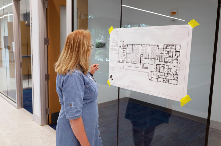 photo of Sandy Redmon A person reviews architectural plans posted on a glass wall inside Scovell Hall.