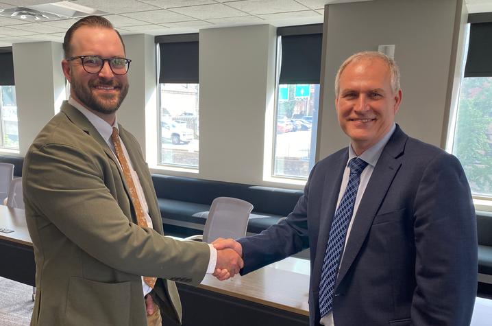 Schaub and Andrews Two adults in business attire shake hands and smile in a conference room. Large windows line the room behind them, highlighting a professional partnership or collaborative agreement.