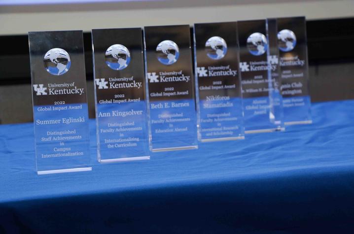 Row of clear glass awards displayed on a blue tablecloth at an event.