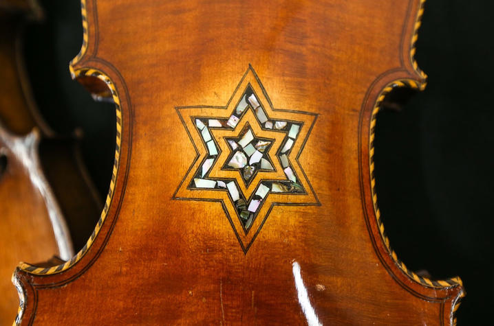 A close-up of the back of a violin featuring an inlaid six-pointed star design made of light-colored decorative materials. The wood has a warm, glossy brown finish with visible grain.