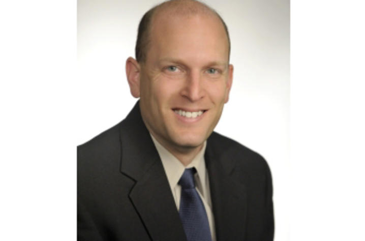 Joshua Douglas faculty portrait wearing a black suit with blue tie on white background