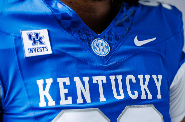 photo of UK Football jersey with UK Invests patch Close-up of a blue football jersey with "KENTUCKY" across the chest, featuring SEC, Nike and UK Invests patches.
