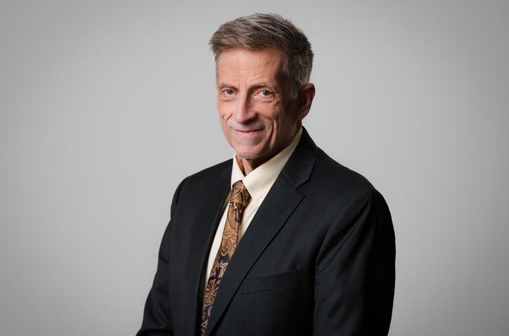 photo of James Donovan Studio portrait of a person wearing a dark suit jacket, light-colored dress shirt and patterned tie against a gray background.