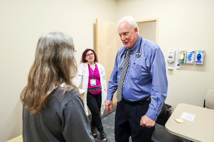 A woman stands in a clinic room with her back to us; she is a clinical trial participant. Facing us is Dr. Gregory Jicha, a doctor and researcher, who's smiling at the participant. 